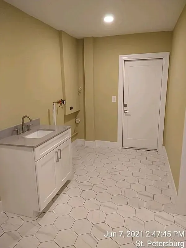 Bathroom with white hexagon tile floor, white vanity and door, beige walls.