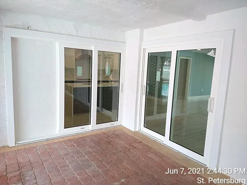 White sliding glass doors on a brick patio. One door is open. The interior is visible.