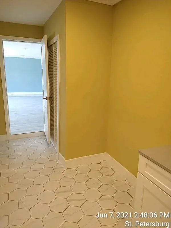 A hallway with hexagonal tile flooring and yellow walls. An open doorway leads to a room with light blue walls.
