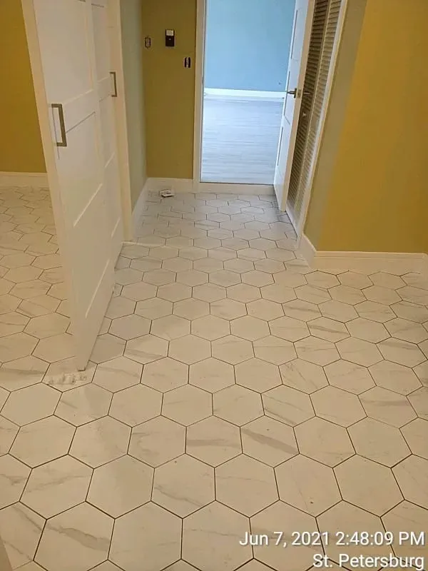 White hexagon-tiled floor in a hallway with white doors, light yellow walls, and a blue-walled room visible.