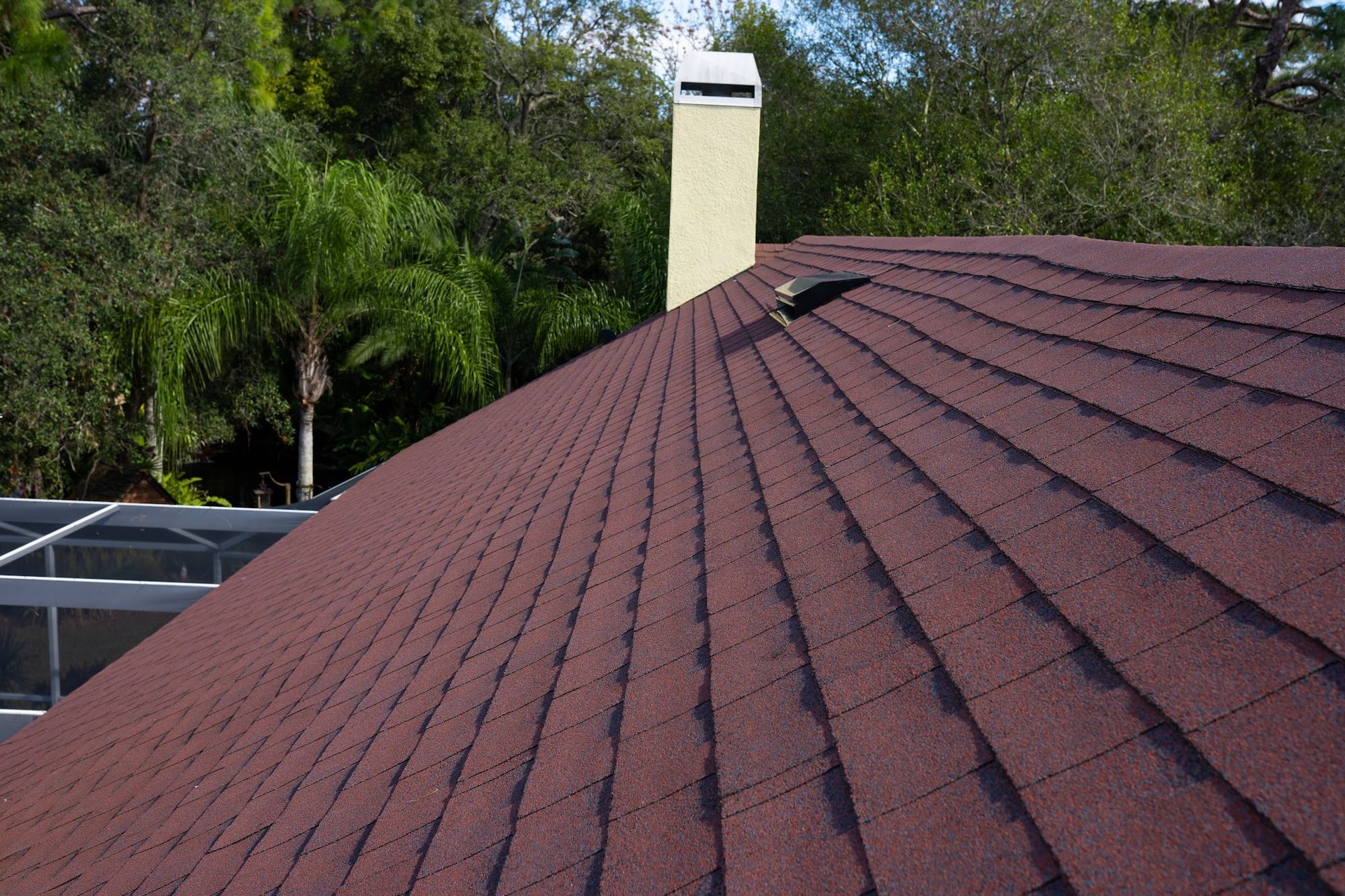 Brown shingle roof with a chimney and surrounding trees.
