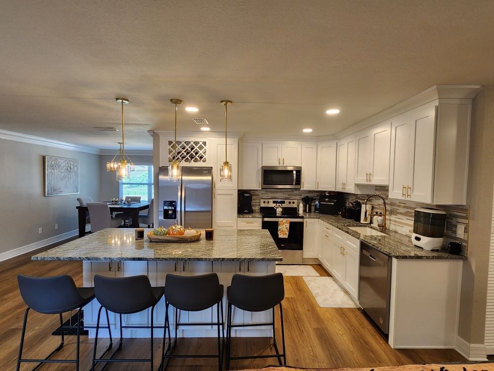 Modern kitchen with white cabinets, granite countertops, island with bar stools, and stainless steel appliances.
