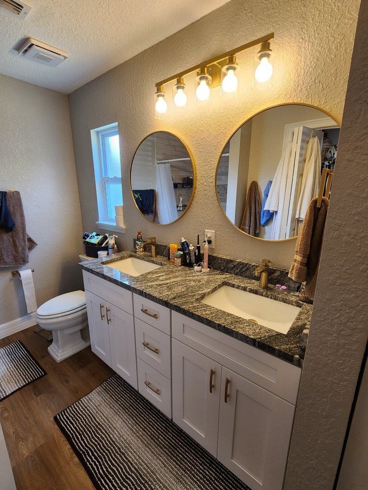 Bathroom with a double sink vanity, gold-framed mirrors, and a light fixture.