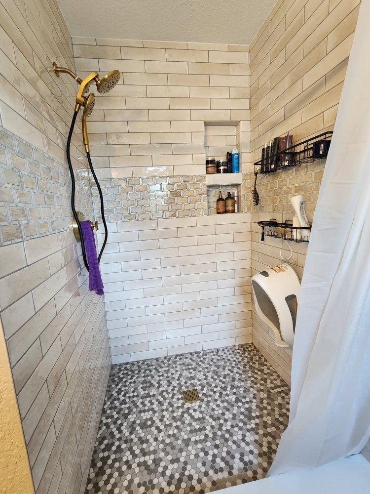 A small shower with textured walls, a pebble floor, and a gold showerhead.