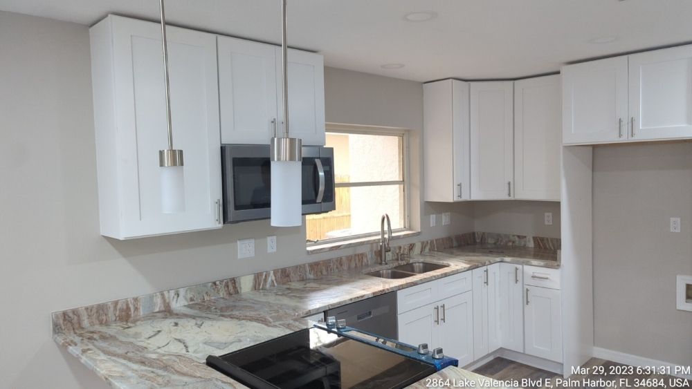 White kitchen cabinets with granite countertops, stainless steel appliances, and a window.