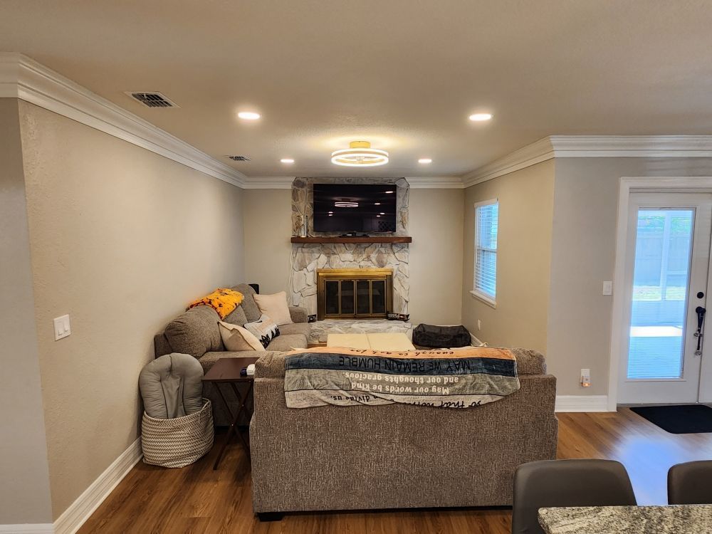 Living room with a couch facing a stone fireplace with a TV. Brown floors and light walls.