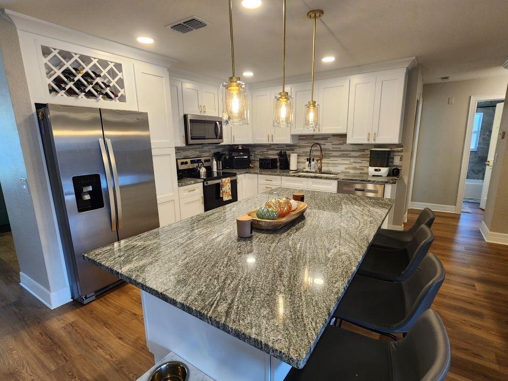 Modern kitchen with white cabinets, gray granite island, stainless steel appliances, and wood floors.