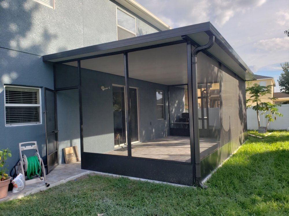 Screened patio attached to a blue house, dark frames, and green lawn.