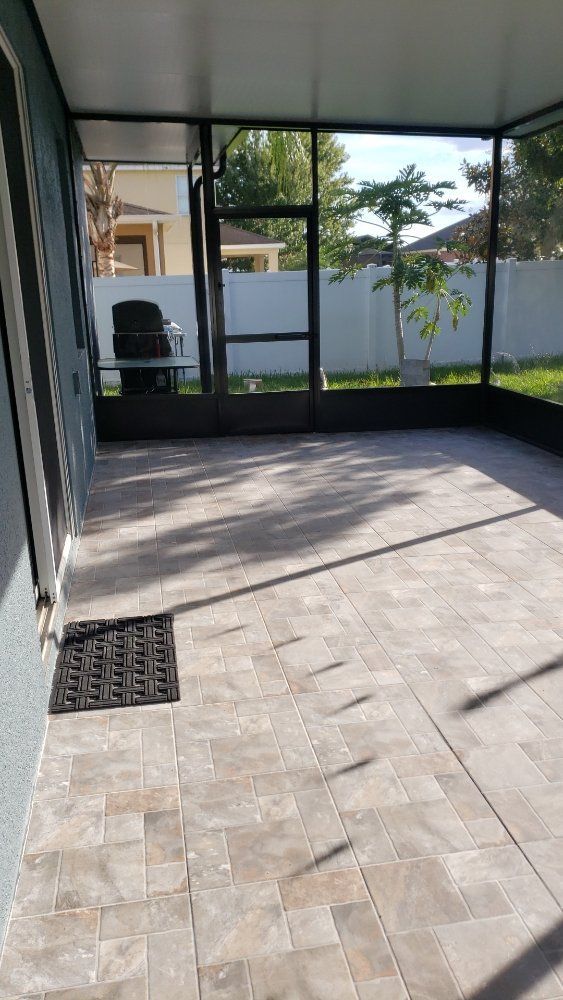 Screened-in patio with brick pavers. Black grilling area visible. Sunny day.