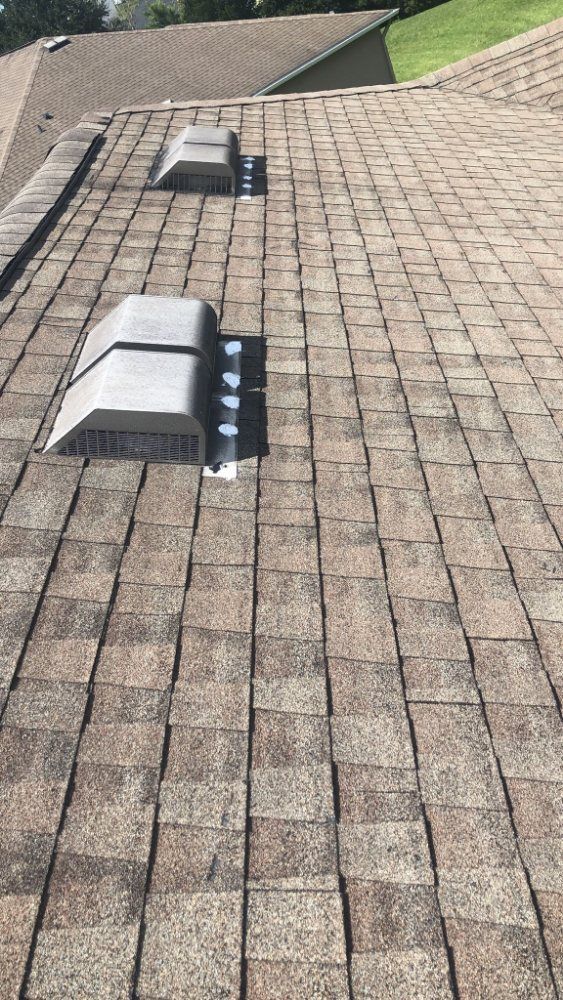 Brown shingled roof with two rectangular vents; sunny, daytime setting.