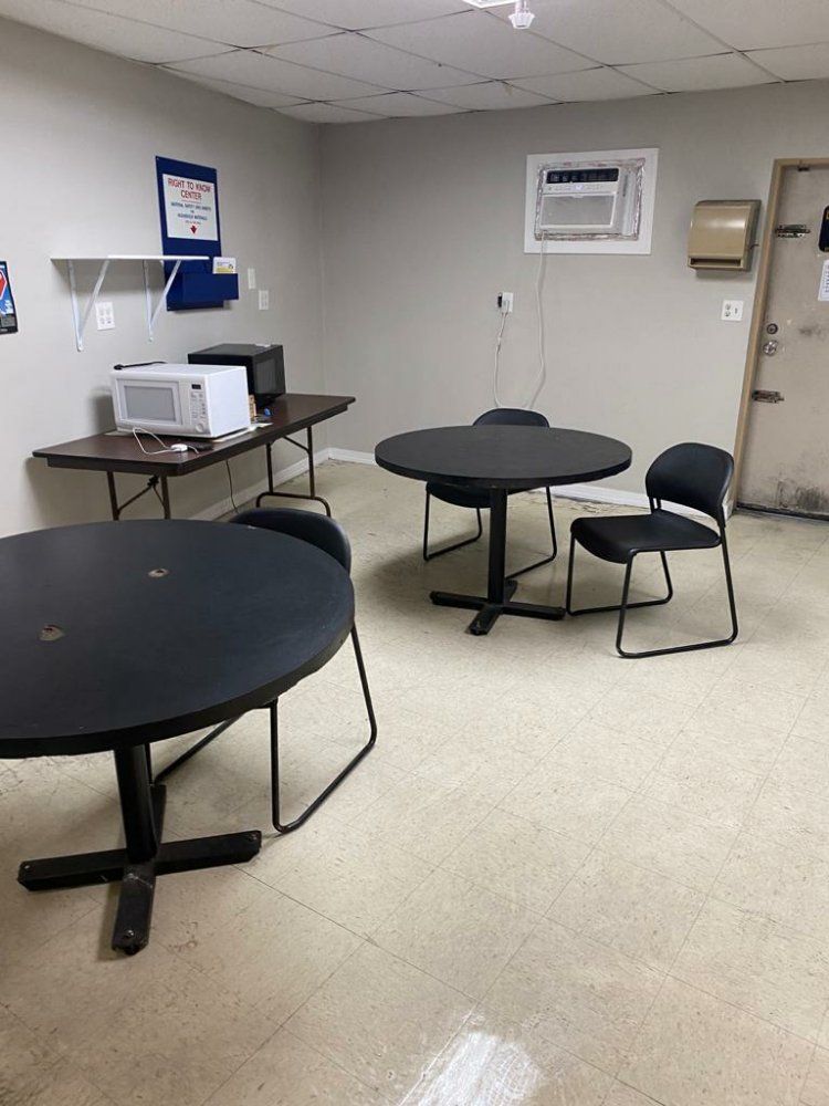 Empty breakroom with two round tables and chairs, a microwave, and a small table with a computer.