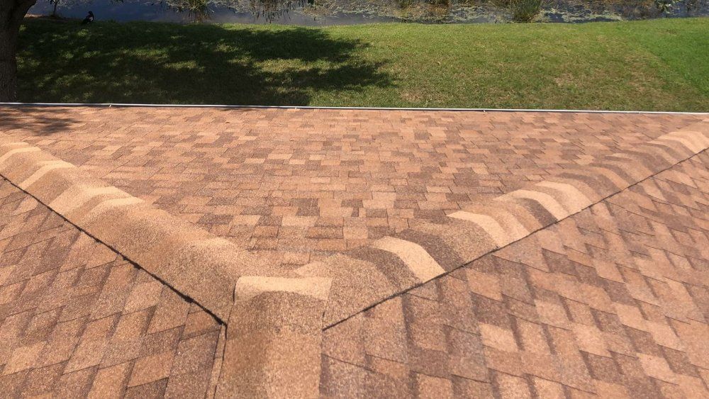 Close-up of brown shingle roof with a V-shaped valley, above a green lawn.