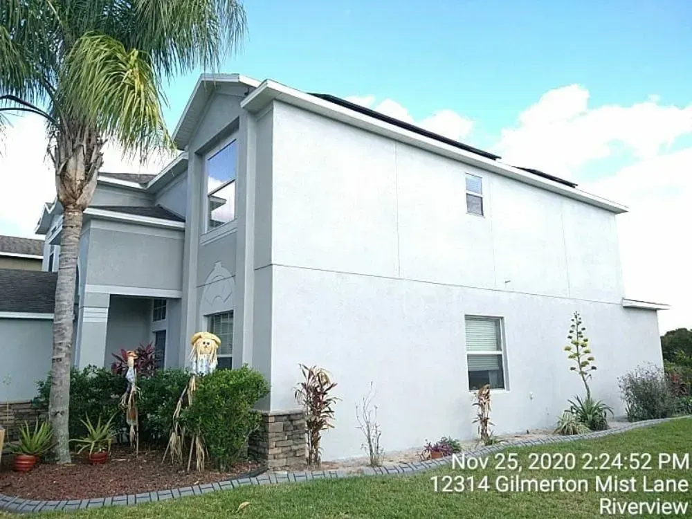 Two-story stucco house with palm tree, landscaping, and a blue sky.
