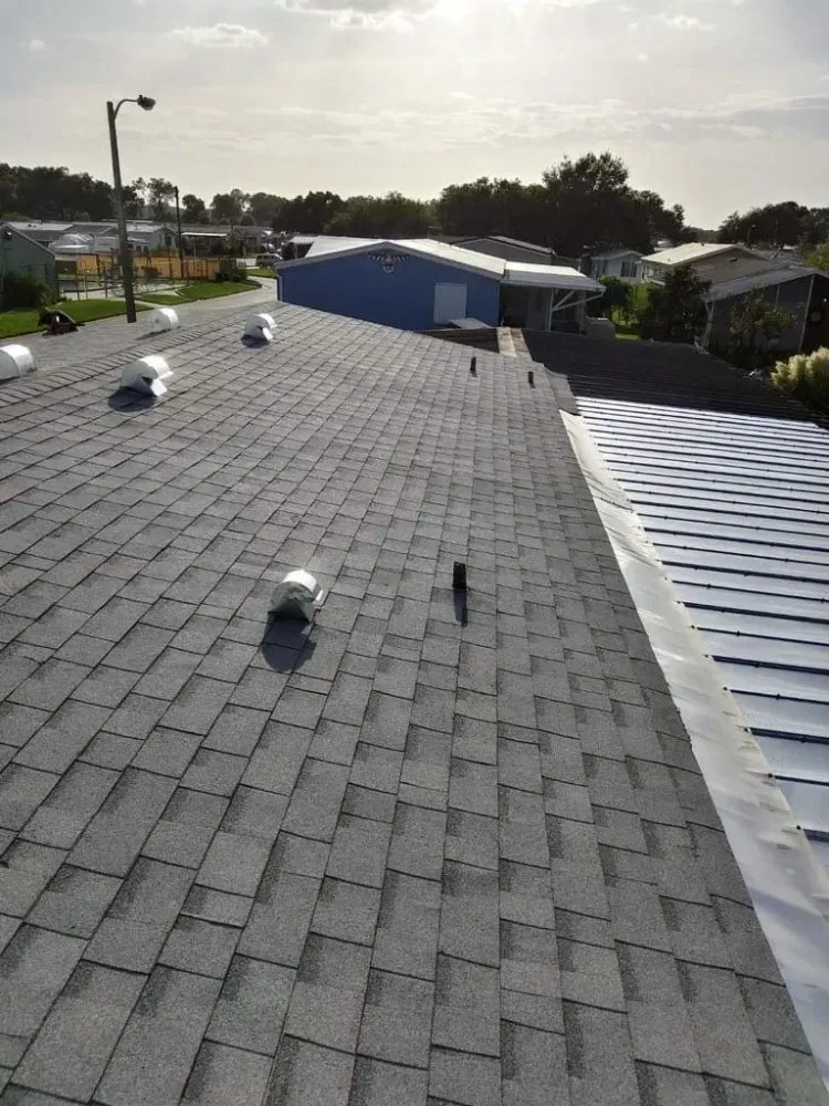 Gray asphalt shingle roof with vents; building in background under sunny sky.