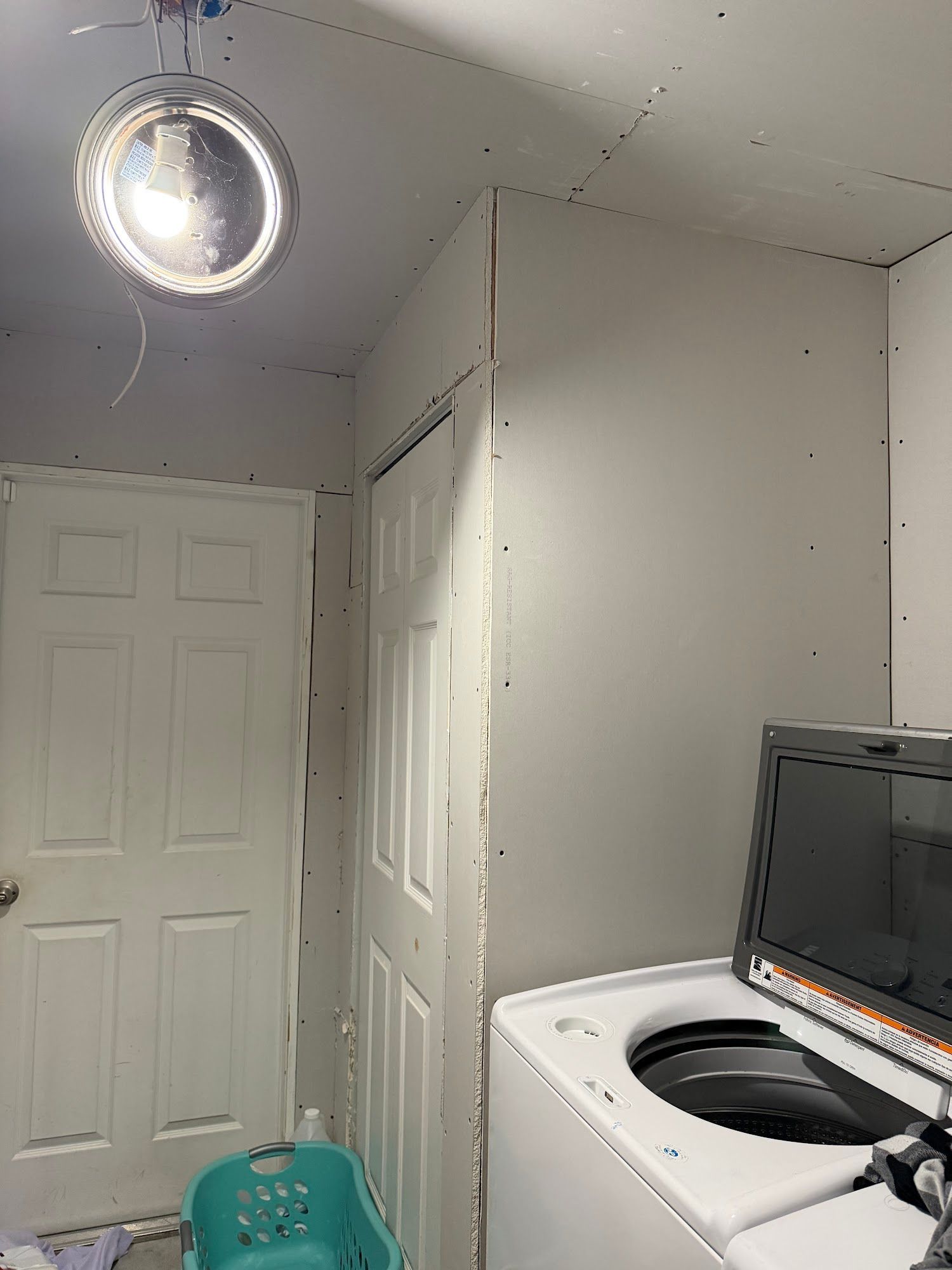 Laundry room with a door, closet, washing machine, and bare drywall walls.