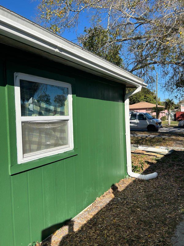 Green building exterior with white trim, window, and gutter. Sunny day.