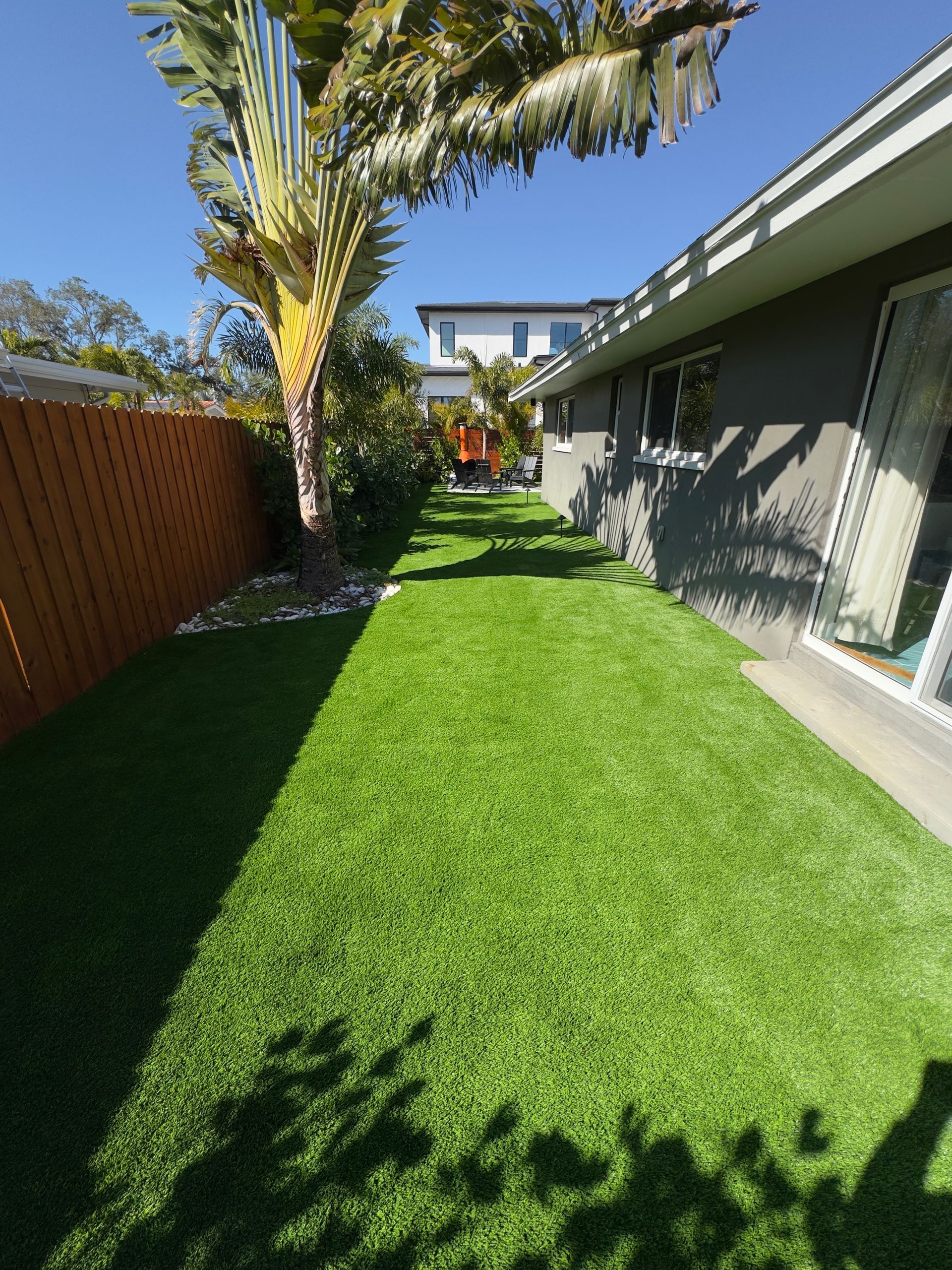 A person rolls out sod onto prepared soil in a yard. Green grass contrasts with the brown earth.