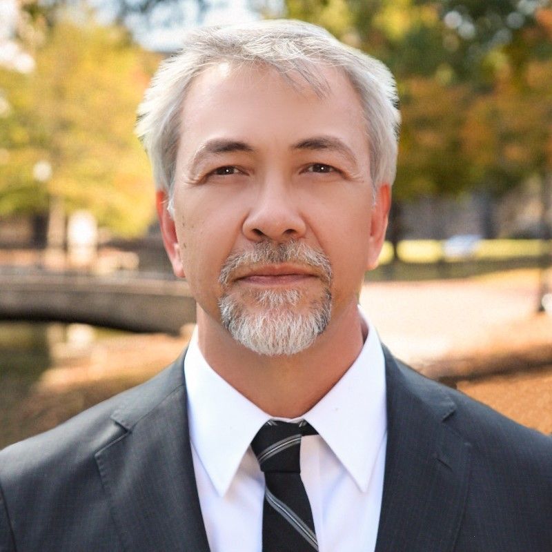 a man in a white shirt is standing in front of a rusty fence .