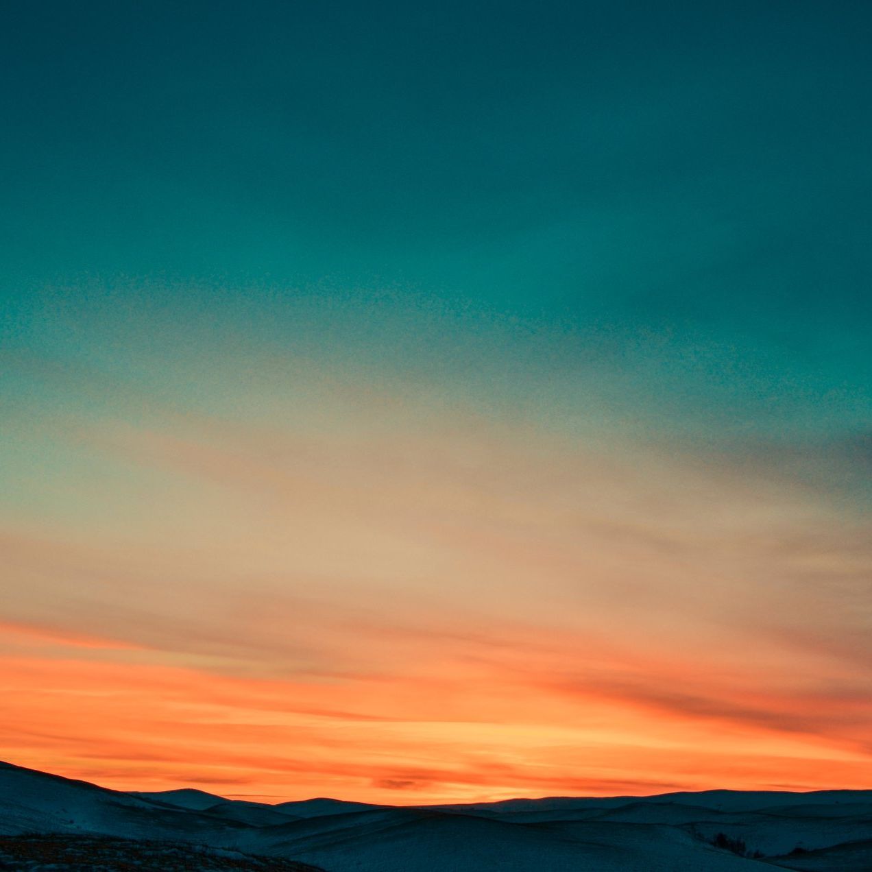 a sunset over a snowy mountain range with a blue sky