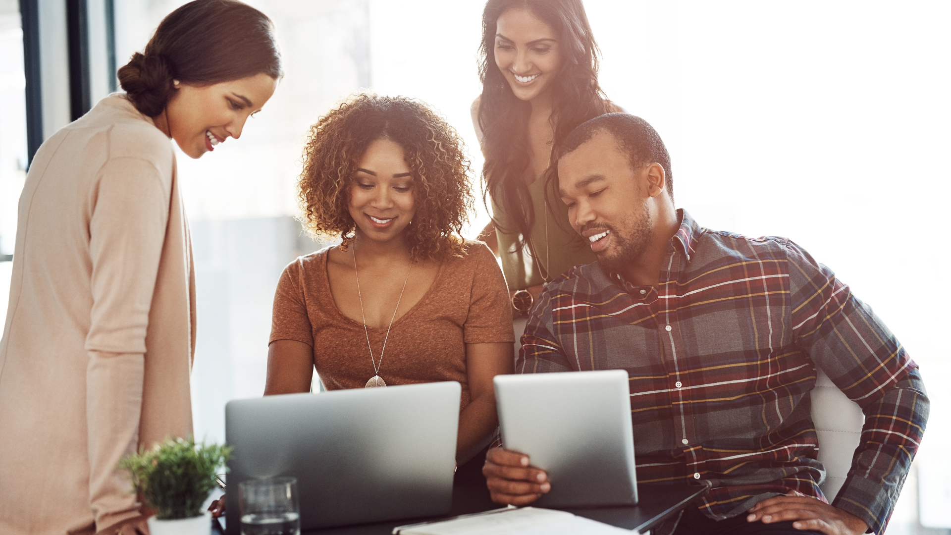 A group of people are standing around a table looking at laptops.