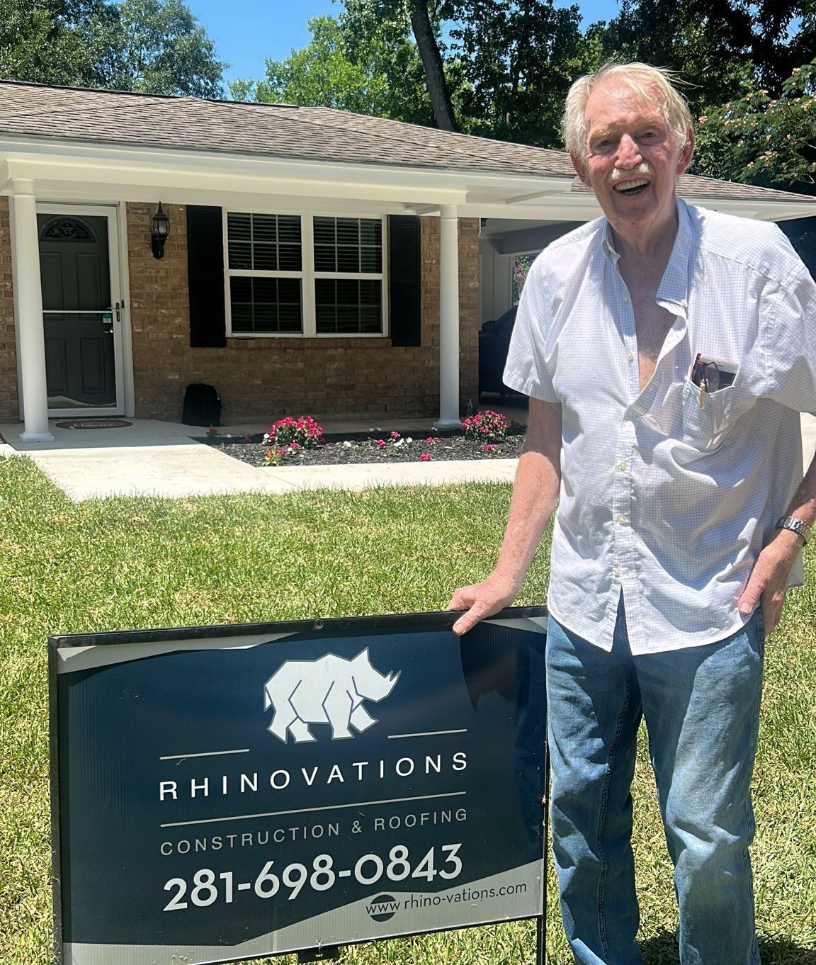 A man is standing in front of a house holding Rhinovations  sign