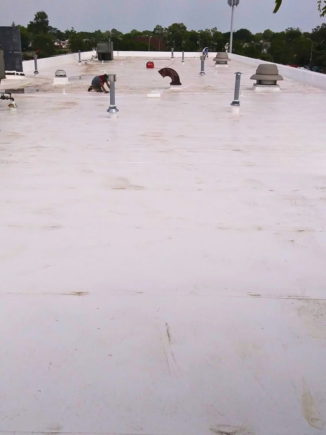 A white, flat commercial roof featuring multiple vents, pipes, and a small red object under an overcast sky.
