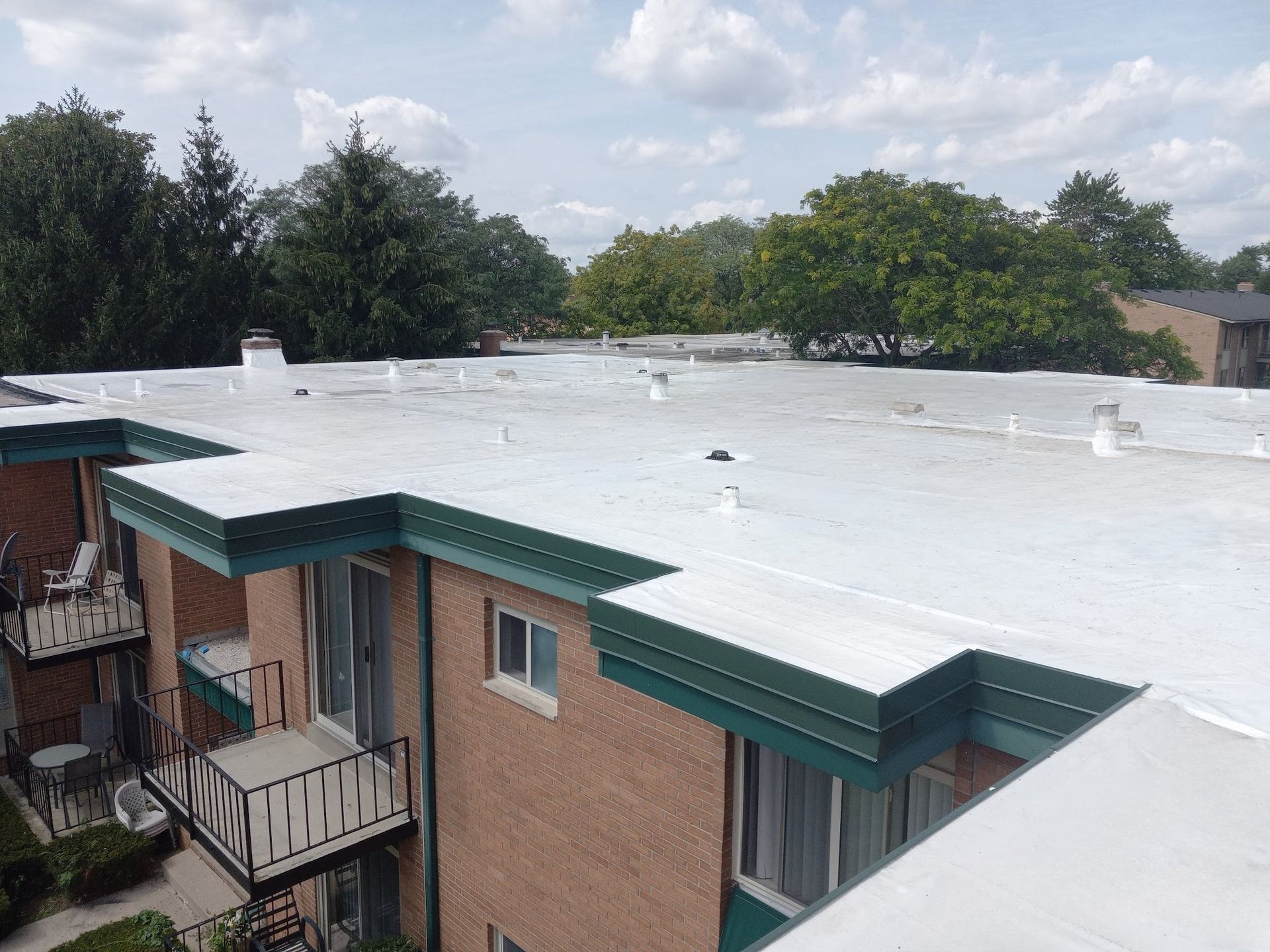 An eye-level shot of a white flat roof on a brown brick apartment building with dark green trim under a cloudy sky.