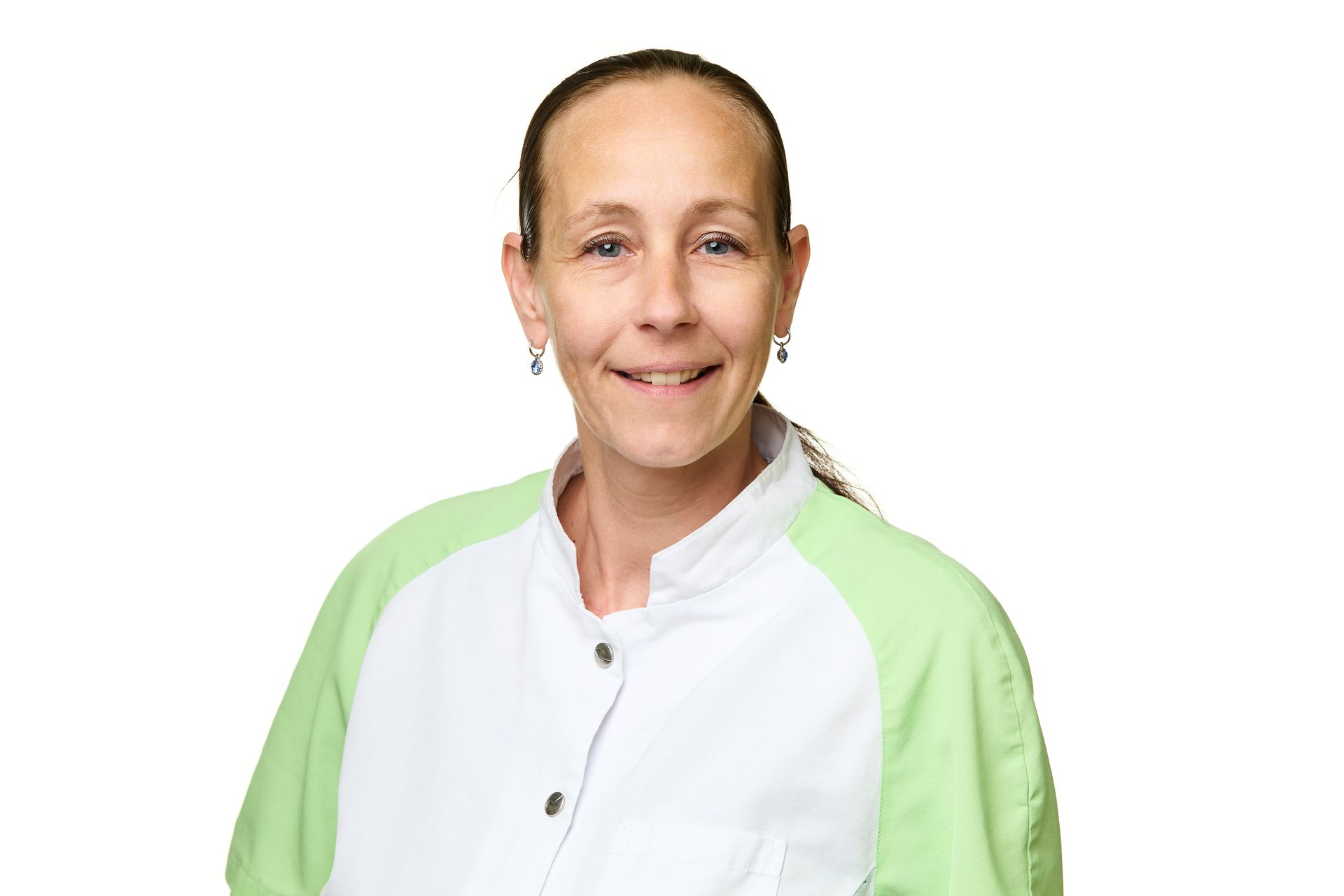 Frau mit heller Haut, trägt einen weiss-grünen Arztkittel und lächelt.