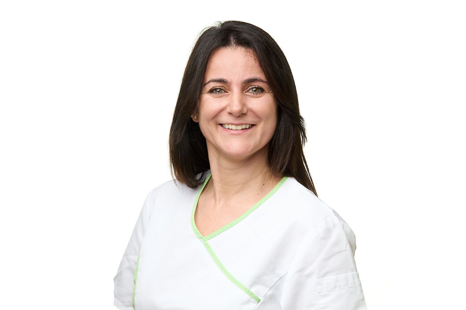 Frau mit dunklem Haar, lächelnd in einem weissen medizinischen OP-Oberteil vor weissem Hintergrund.