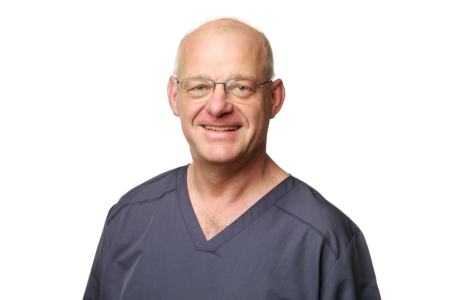 Glatzköpfiger Mann mit Brille und blauem Kittel lächelt in die Kamera.