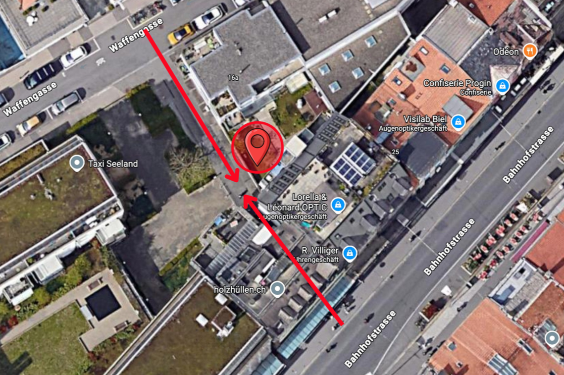 Luftaufnahme eines mit einer roten Stecknadel markierten Ortes. Zwei rote Linien kennzeichnen Wege; Gebäude und Autos sind ebenfalls zu sehen.