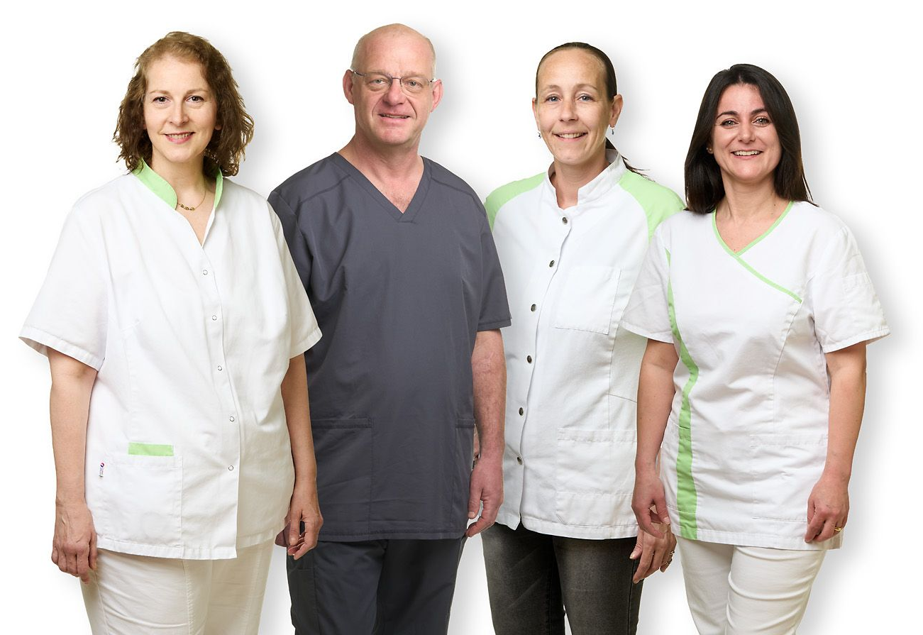 Vier lächelnde Angehörige der Gesundheitsberufe in OP-Kleidung und weissen Kitteln stehen vor einem weissen Hintergrund.