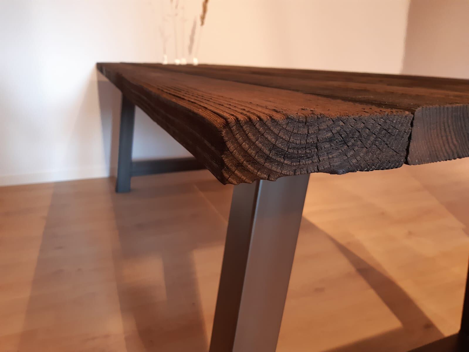 Een houten tafel met metalen poten staat op een houten vloer.