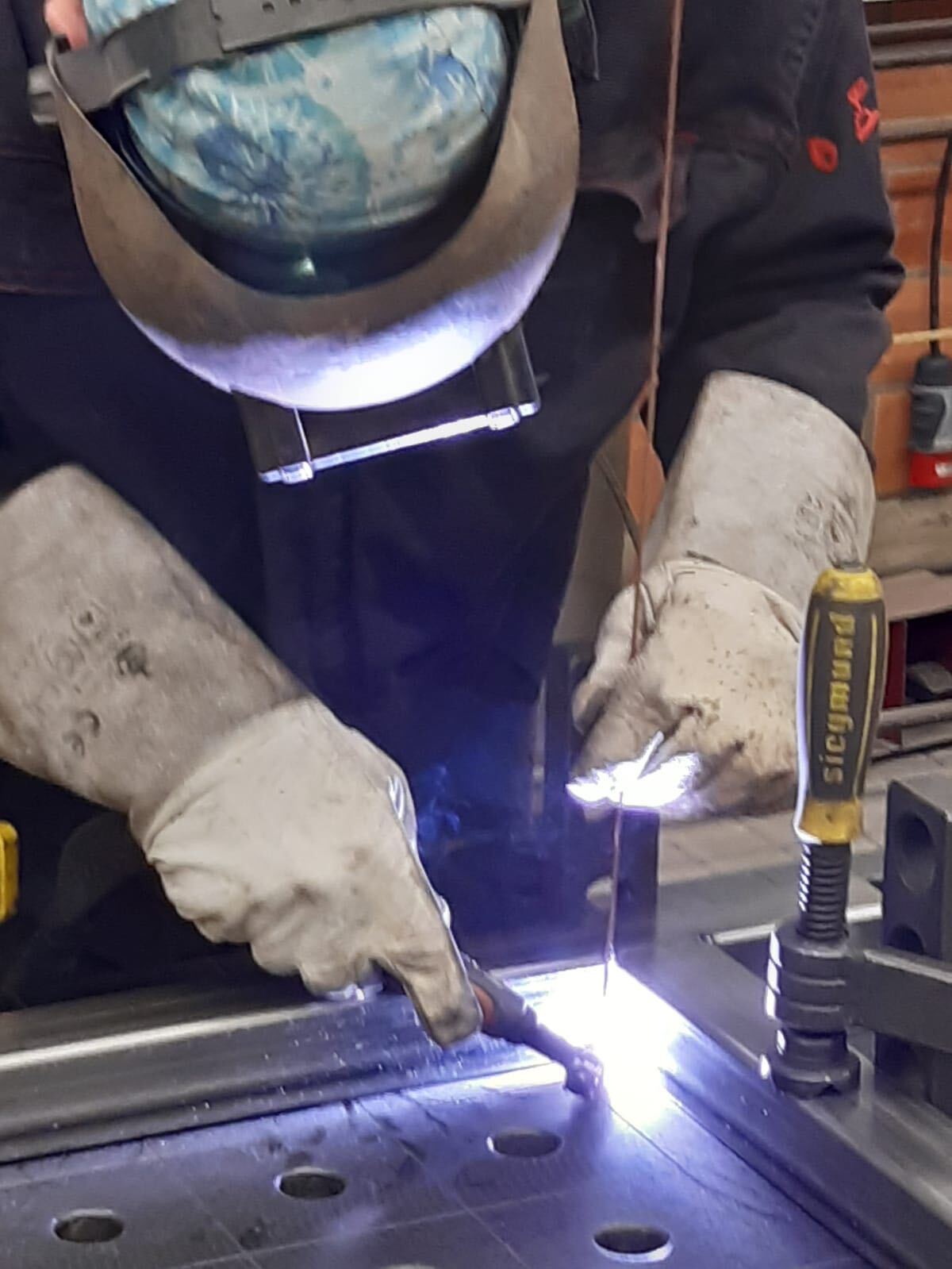 Een man met een lashelm is bezig met het lassen van een stuk metaal