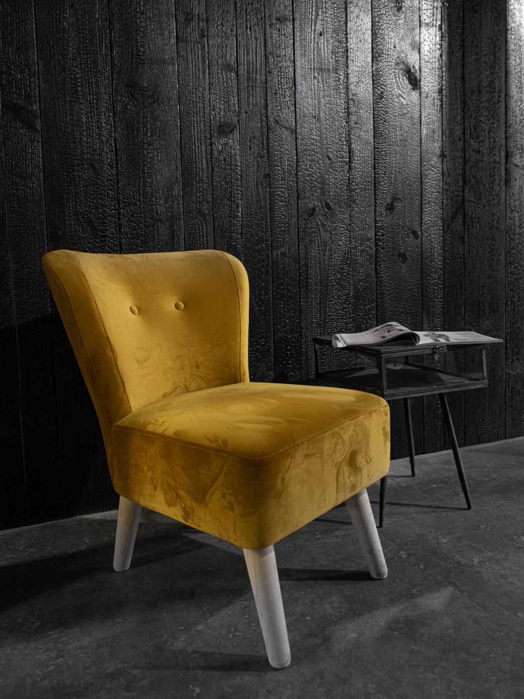 Op een zwart-witfoto staat een gele stoel naast een klein tafeltje voor een shou sugi ban wand.