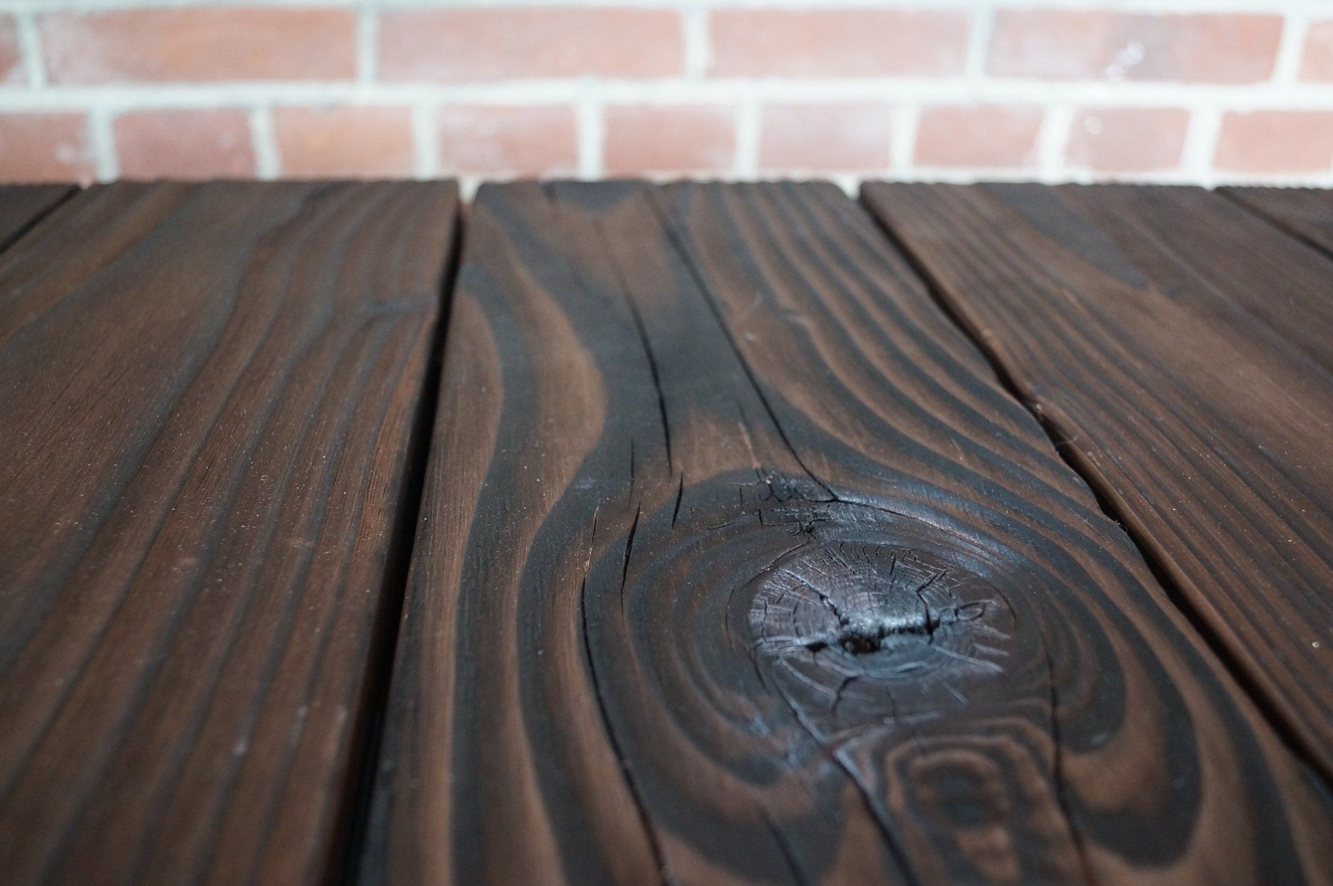 Een close-up van een houten shou sugi ban tafel met een bakstenen muur op de achtergrond.