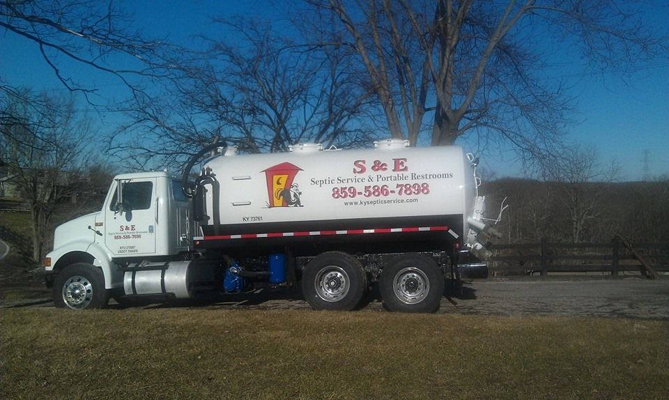 A white vacuum truck is parked in a grassy field