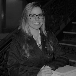 A woman wearing glasses is smiling in a black and white photo.
