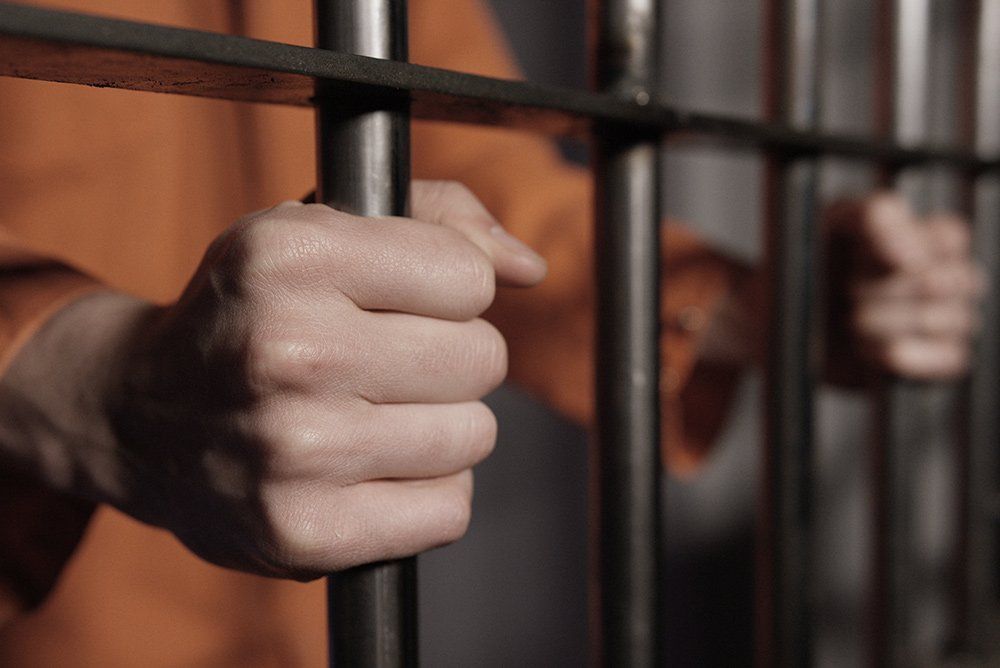 A man in an orange prison uniform is holding onto a prison cell.