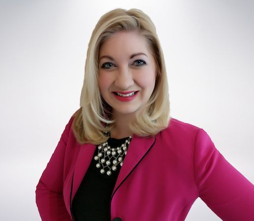 A woman wearing a pink jacket and black top smiles for the camera