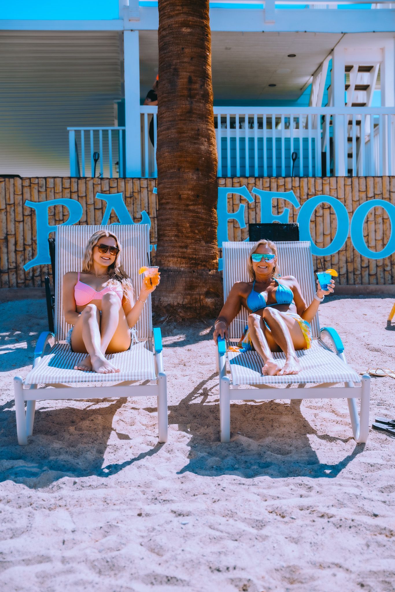Two women are sitting in lounge chairs on the beach.