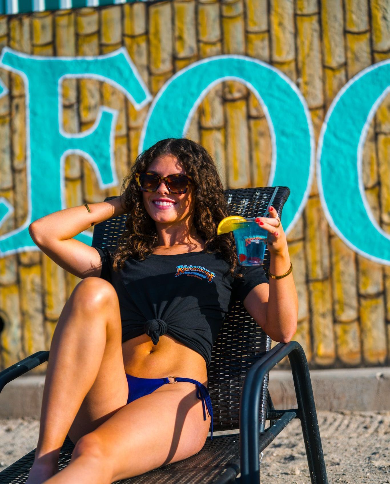 A woman in a bikini is sitting in a chair holding a drink