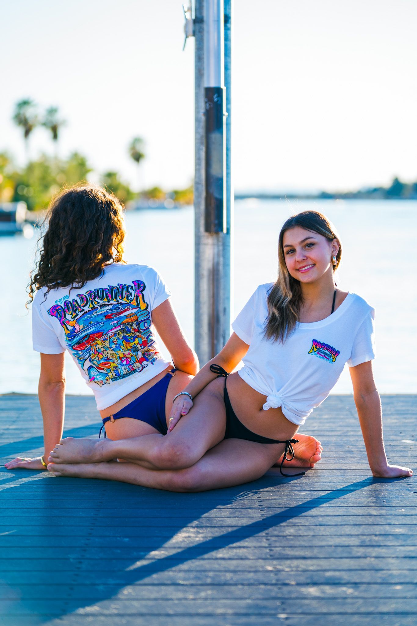 Two women in bikinis are sitting on a dock.