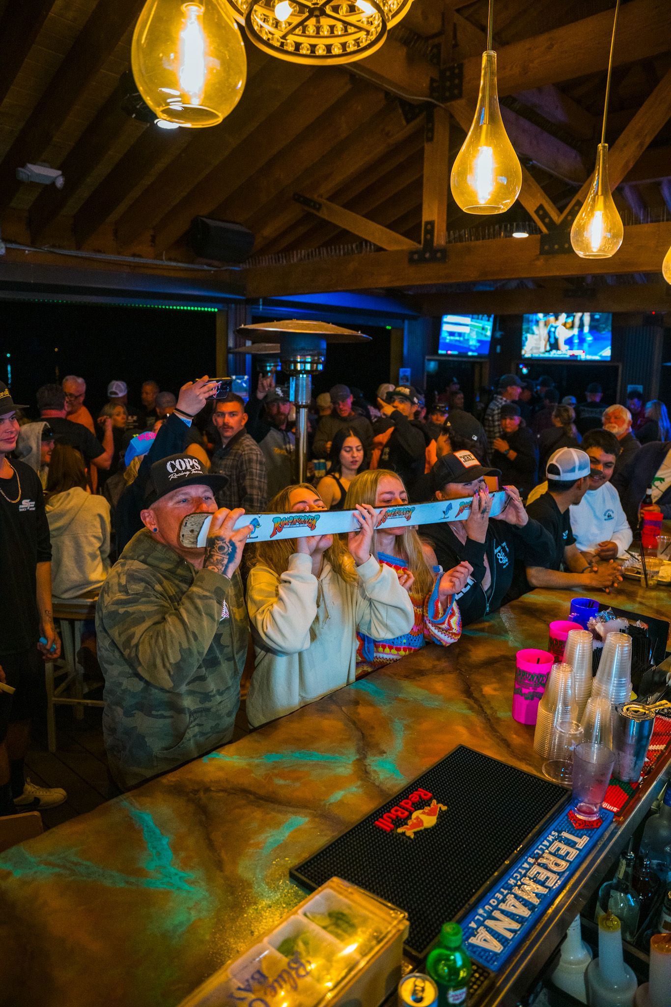 A group of people are sitting at a bar taking pictures with their cell phones.