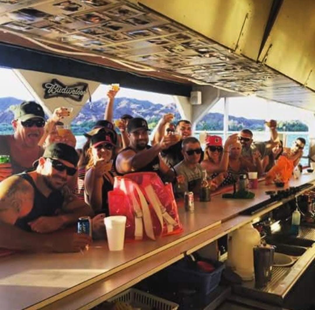 A group of people sitting at a bar with a budweiser logo on the ceiling