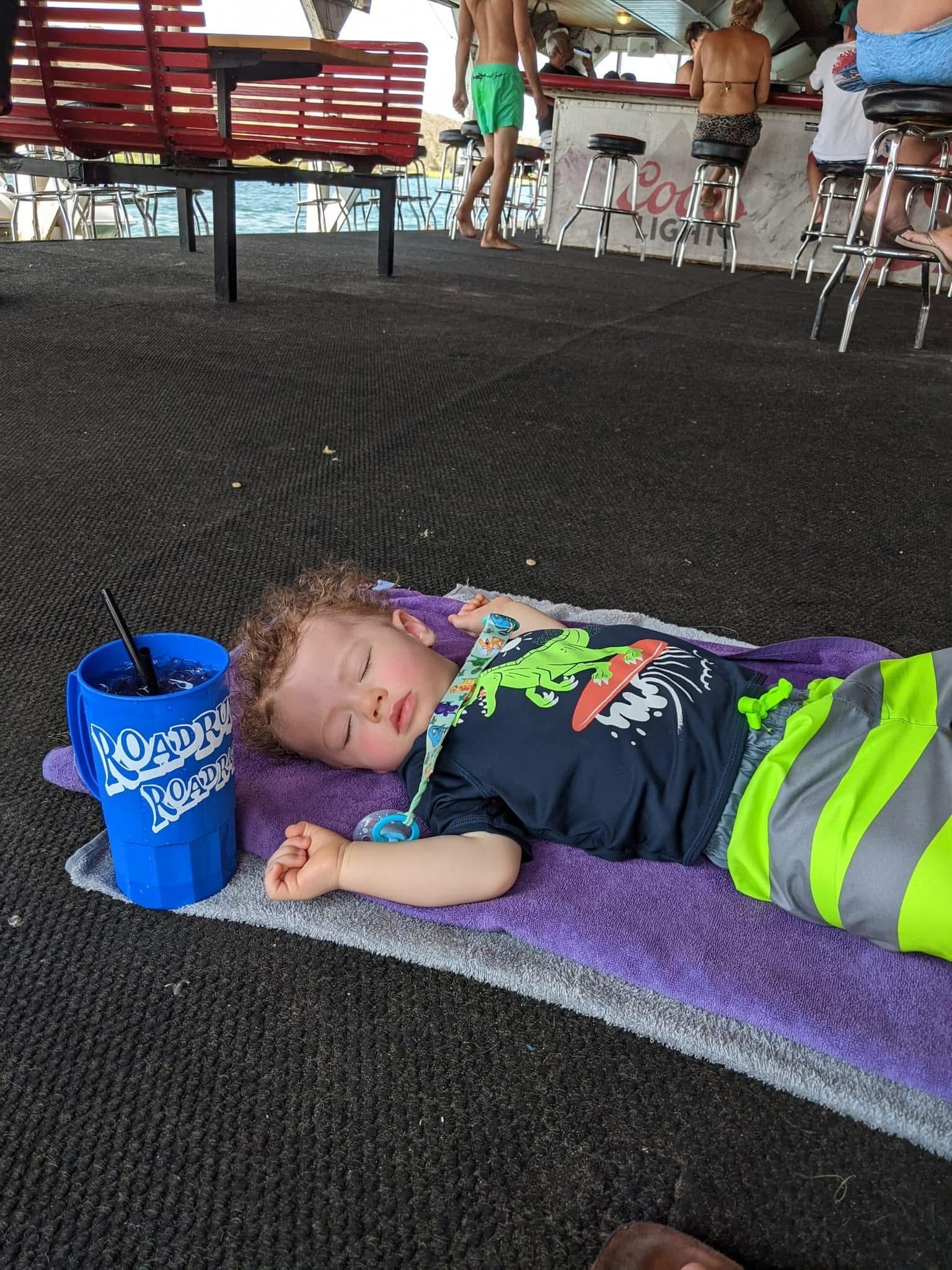 A young boy is laying on a towel next to a blue cup.