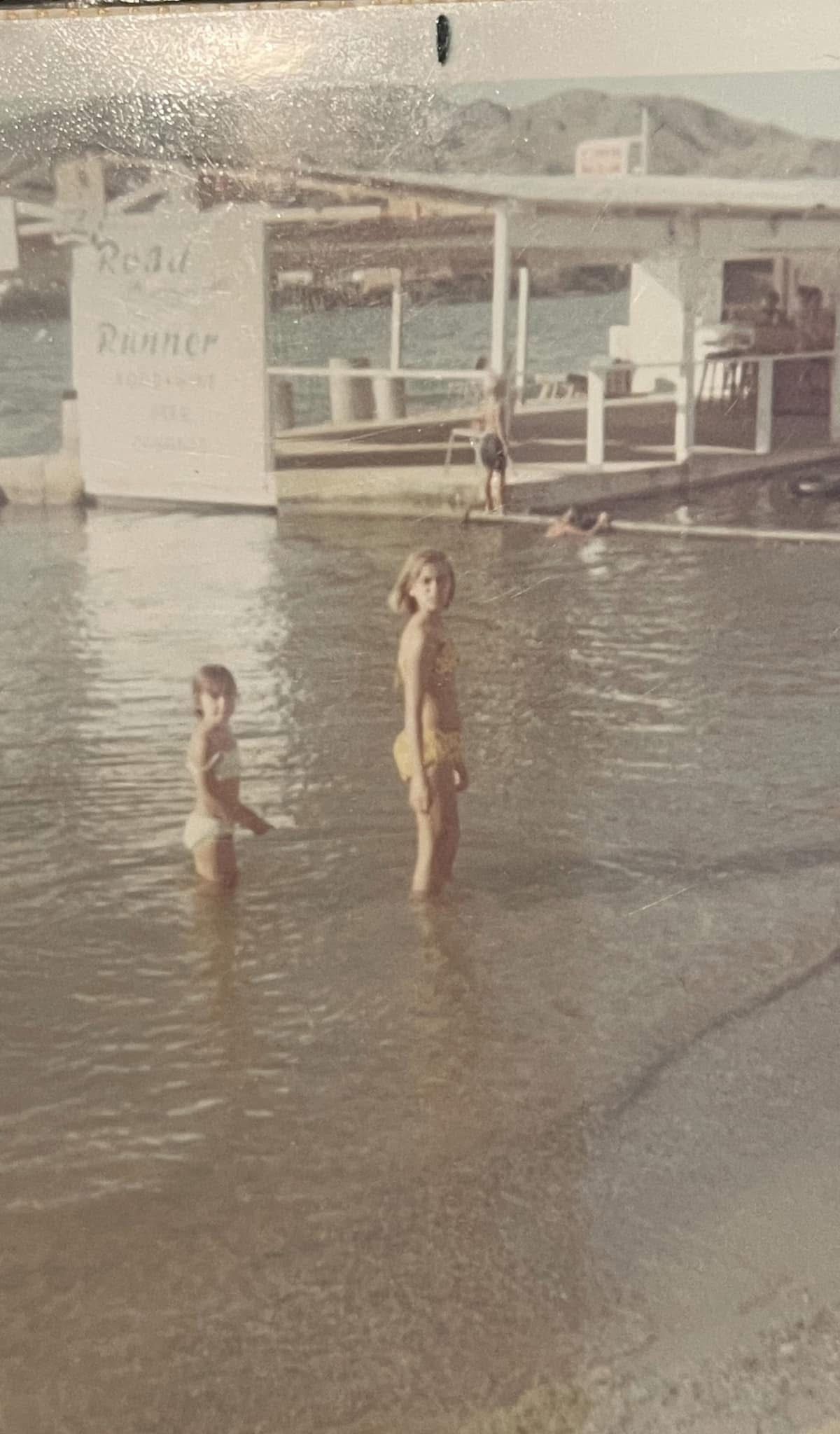 Two children are standing in the water near a dock.