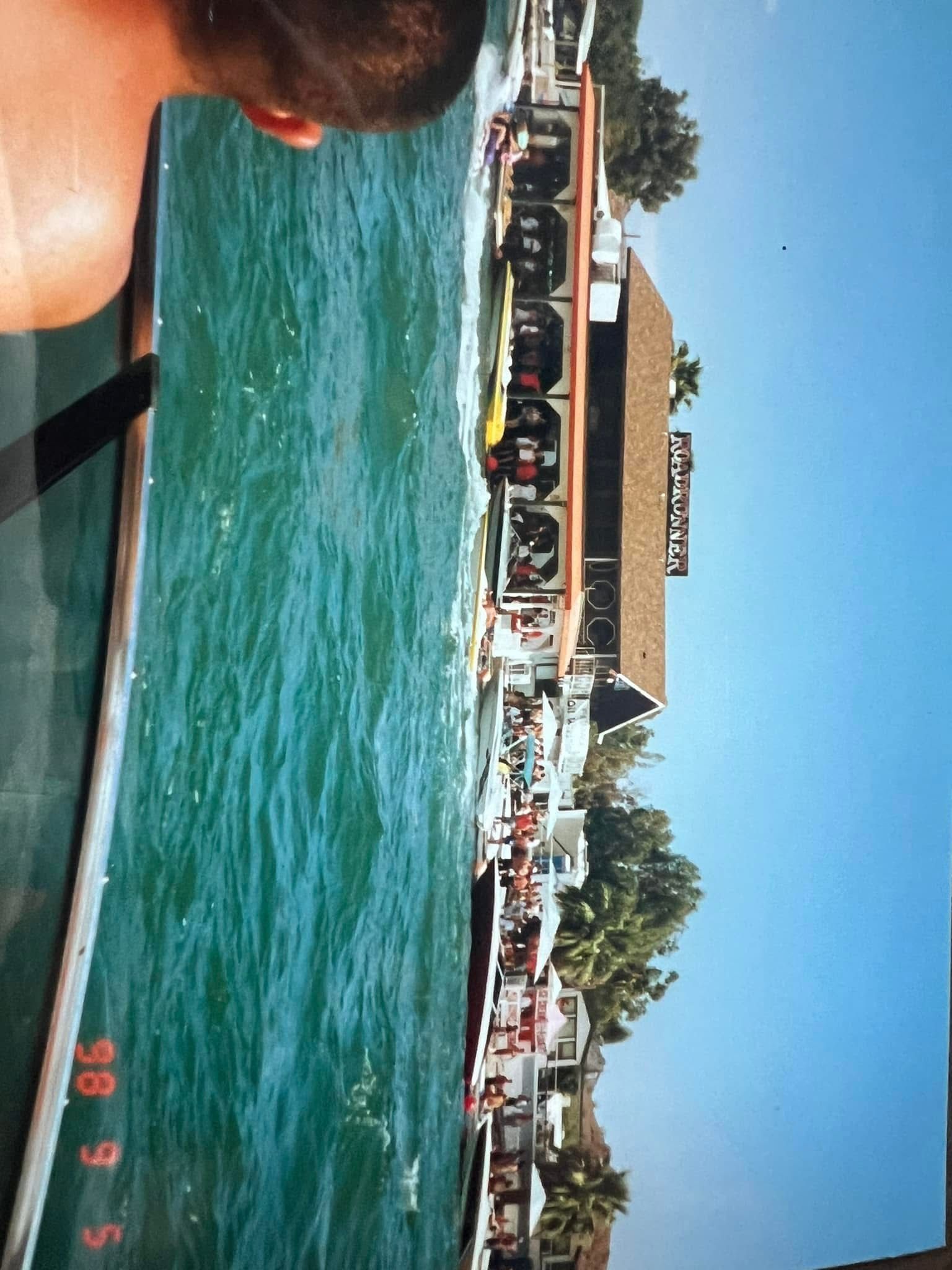 A man is swimming in the water with boats in the background