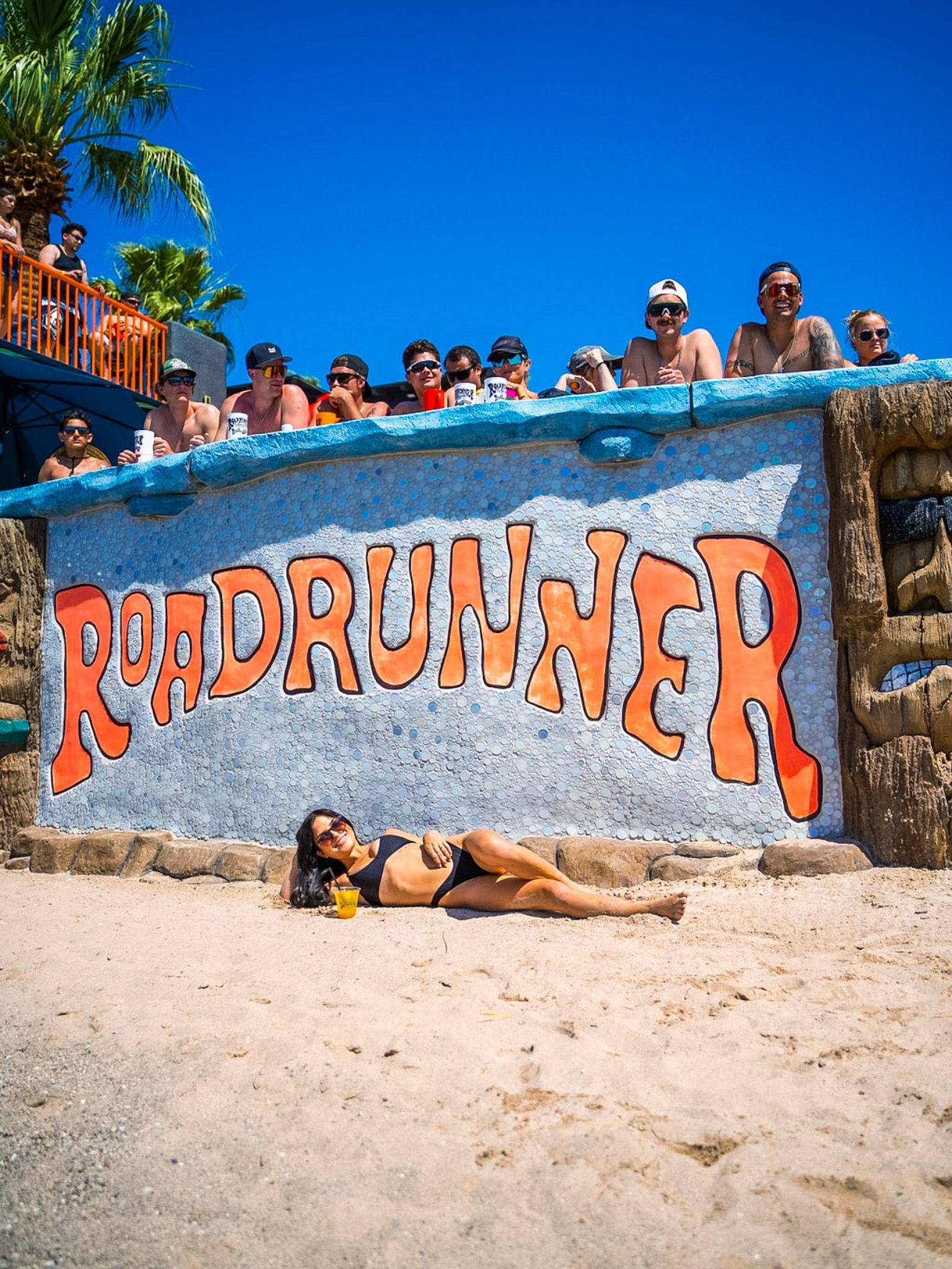 A woman is laying on the beach in front of a sign that says roadrunner.