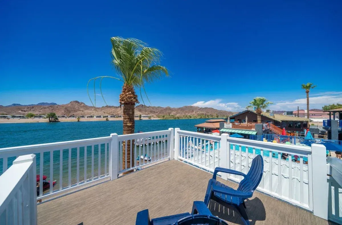 A balcony overlooking a body of water with chairs and a palm tree.